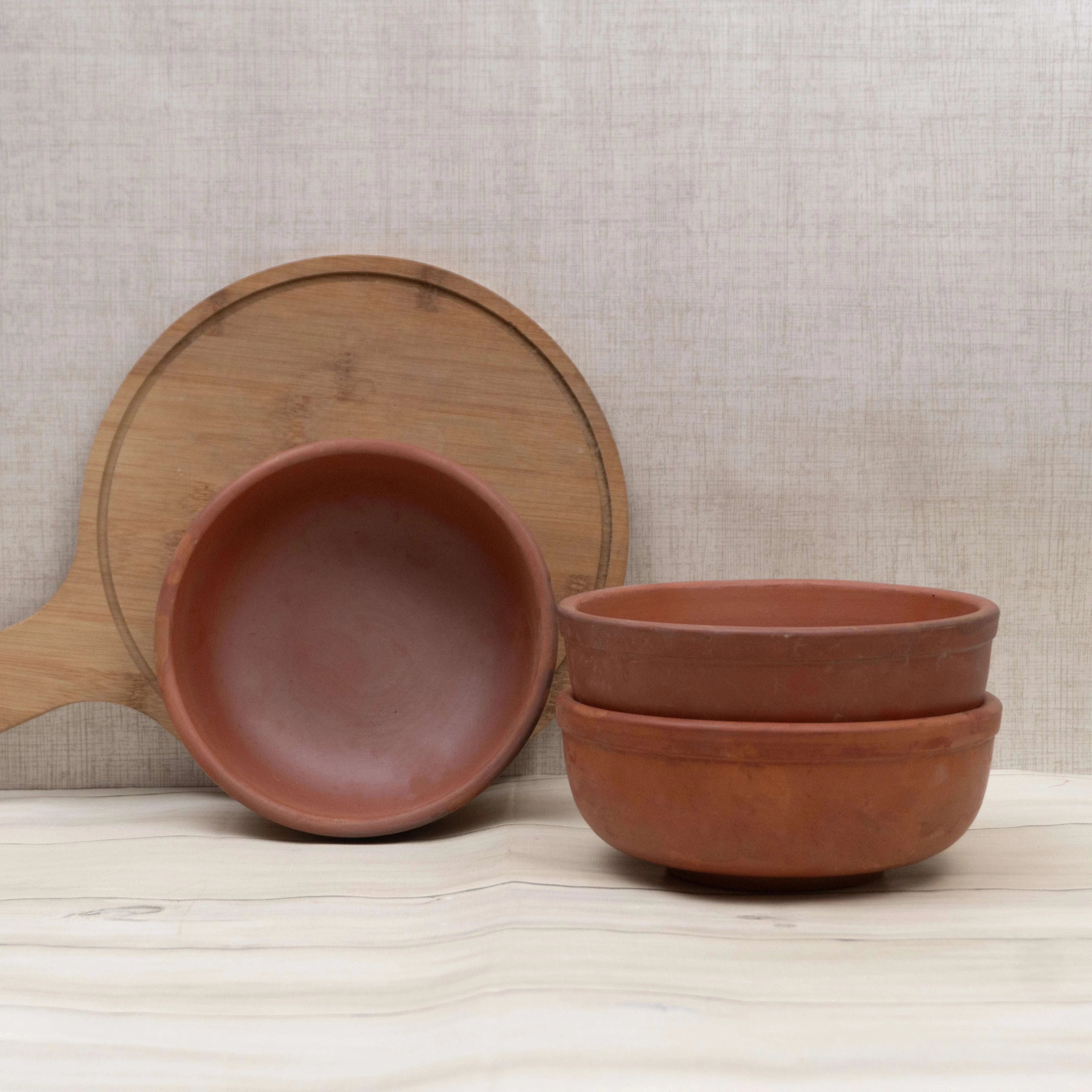 Set of terracotta bowls and a wooden ladle on a neutral background
