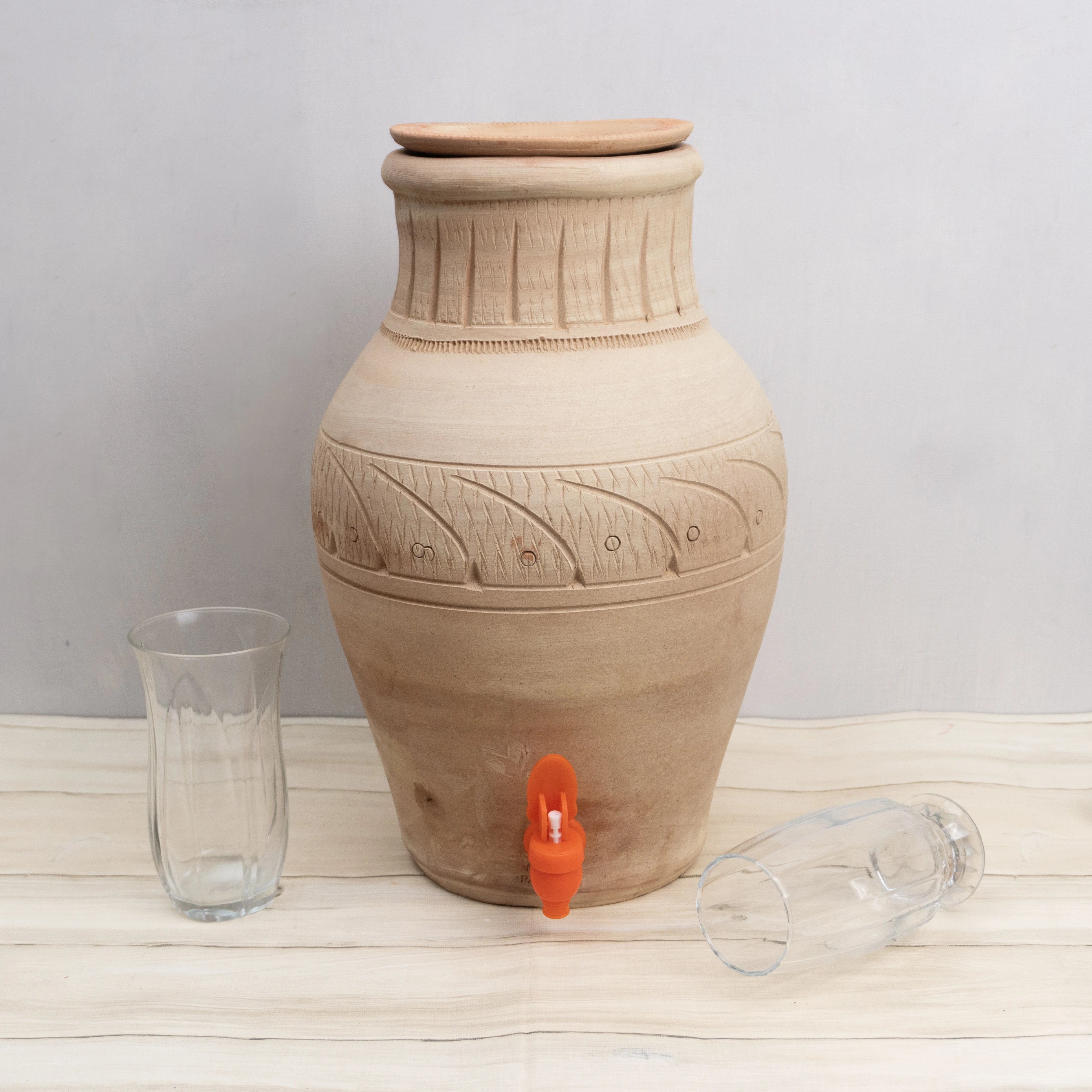 Terracotta water dispenser with decorative patterns on a wooden surface.