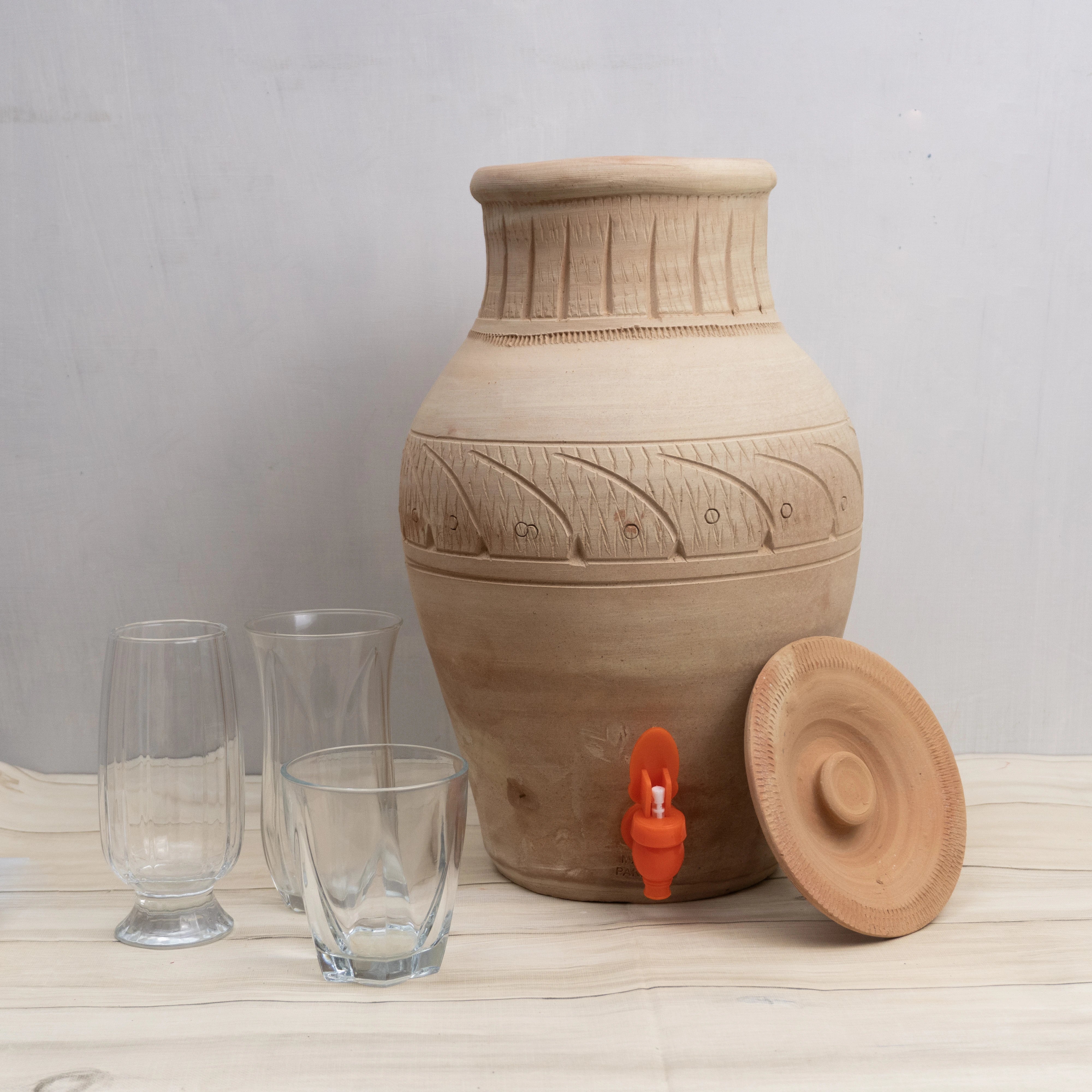 Terracotta water dispenser with glassware on a light surface